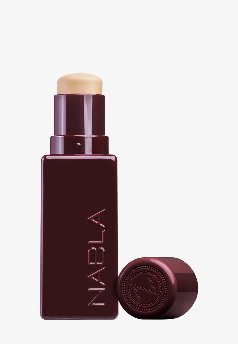 Maroon rectangular stick foundation container with a cream-colored top. Features embossed logo detail on the base. Smooth, glossy finish.