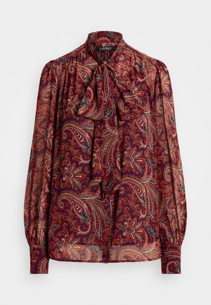 Langærmet gennemsigtig bluse med rødt paisley-mønster, højt halsbånd med sløjfe og rynkede manchetter på hvid baggrund.