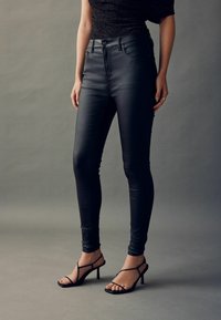 Blugi skinny negri cu talie înaltă, realizați dintr-un material elastic, având detalii subtle de cusătură, asortați cu sandale negre cu curele.