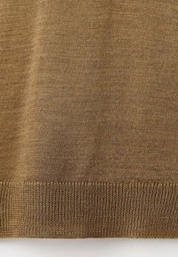 Kratak prikaz smeđeg pletenog materijala koji prikazuje fine detalje šavova i rebrasti donji rub.