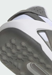 Šedá a biela športová obuv s textúrovanou podrážkou, hornou časťou z mriežkového materiálu a suchým zipsom. Zvýšený podpätok s charakteristickým vzorom.