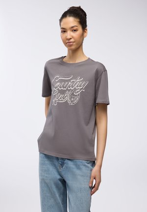 T-shirt in cotone grigio a maniche corte, con una grafica bianca "Country Girl". Texture liscia, vestibilità comoda, abbinato a jeans azzurri chiari.