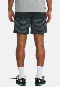 Shorts de sport noirs avec des rayures blanches horizontales, en tissu léger et avec une taille élastique, accompagnés de chaussures noires et de chaussettes blanches.