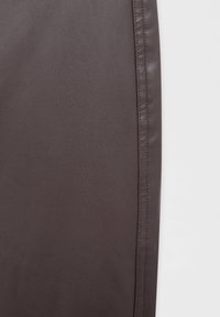 Mörkbrun lädertextil med synlig fin korntextur och sömstygn längs den högra kanten mot en enfärgad vit bakgrund.