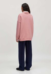 Roze oversized sweatshirt met verlaagde schouders, geribde manchetten en een afgeronde zoom, gecombineerd met donkerblauwe wijde pijpen.