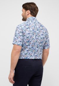 Camicia a maniche corte con un motivo floreale blu su uno sfondo chiaro, caratterizzata da un colletto classico e un design a taglio dritto.