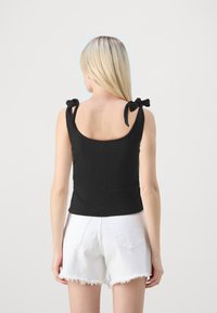 Débardeur noir à côtes avec un dos arrondi et des bretelles à nouer réglables. Associé à un short en denim blanc déchiré, mettant en avant un style décontracté.