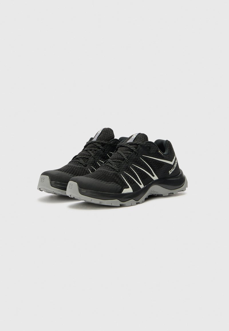 Schwarze Sportschuhe mit einer strukturierten Oberseite, grauer Laufsohle und reflektierenden Akzenten. Verfügt über einen Schnürverschluss und markante Seitendesigns.