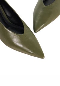 Pointed-toe pumps made of smooth, olive green leather with a sleek silhouette and black interior lining, featuring a minimalist design.