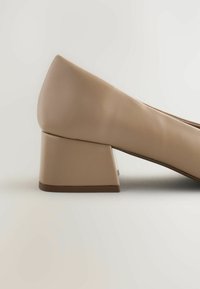 Pantof bej cu toc înalt cu bloc triunghiular, textură netedă de piele și design cu vârf rotunjit.