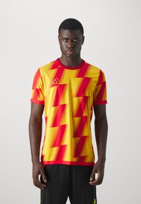 Rode en gele sporttrui met korte mouwen, voorzien van een zigzagpatroon, ronde hals en Adidas-logo op de linkerborst. Gladde textuur.