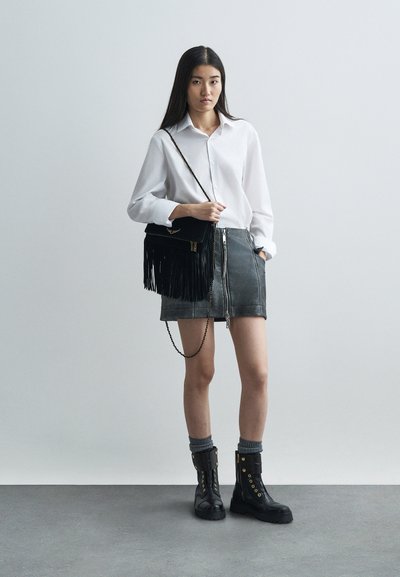 Black leather skirt with a front zipper, paired with a white button-up shirt. Black ankle boots and a black fringed crossover bag.