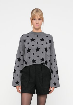 Sweater court gris avec un motif d'étoiles noires, encolure ronde et manches larges, porté sur un short noir texturé. Finition tricot lisse.