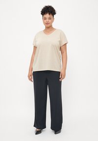 Beige v-veida t-krekls ar īsām piedurknēm, kas apvienots ar garām melnām biksēm. Strukturēta auduma brīvs piegriezums. Polka punktu apavi pabeidz komplektu.