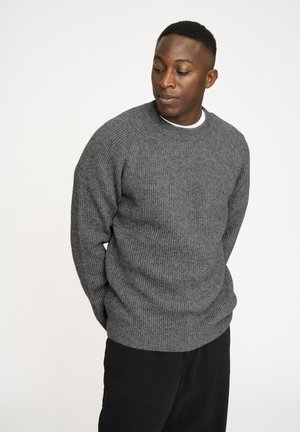 Grå ribbet sweater med rund halsudskæring, lange ærmer og løs pasform, parret med mørke bukser. Glat tekstur og enkelt design.
