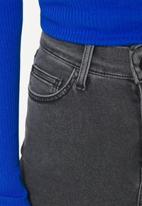 Jeans negros de talle alto con un diseño clásico, que incluyen un bolsillo frontal, una cremallera con botón y una textura suave. Combinados con una blusa azul de canalé.