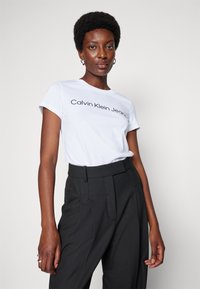 Witte katoenen t-shirt met korte mouwen met het "Calvin Klein Jeans" logo in het zwart. Gecombineerd met hoge zwarte broeken.