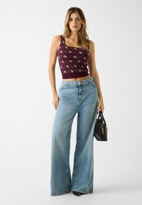 Bordeauxrode gebreide cropped top met ruitmotief, gecombineerd met lichtblauwe wijde jeans. Model draagt een kleine zwarte handtas.