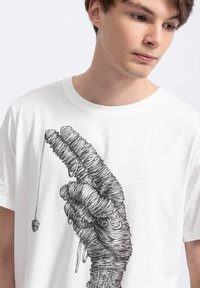Witte katoenen t-shirt met een gedetailleerde zwarte lijntekening van een hand, intricately weergegeven met lussen en stiksels.