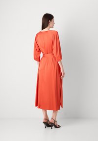 Rochie portocalie, dintr-un material asemănător mătăsii, cu o croială relaxată, mâneci 3/4 și un cordon la talie. Are slituri laterale și cade sub genunchi. Este purtată cu tocuri negre cu bretele.