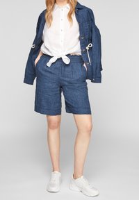 Pantalones cortos de mezclilla con cintura elástica y lazo, con dos bolsillos laterales. Combinados con una camisa blanca de botones y zapatillas deportivas.