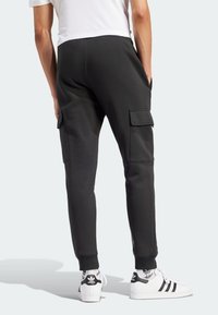 Svarta joggbyxor med cargofickor, elastiska muddar och en slät tygtextur. Matchas med vita sneakers med svarta detaljer.