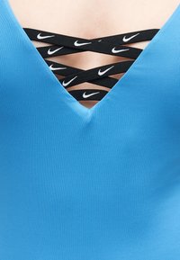 Μπλε ρούχο με V-λαιμόκοψη και μαύρους λουριά σε σχήμα σταυρού με λευκά λογότυπα Nike στο στήθος.