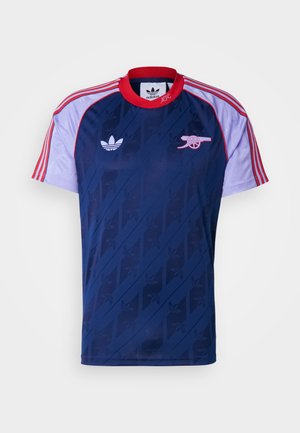 Sportskog majica mornarsko plave boje s kontrastnim rukavima u crvenoj i svijetlo ljubičastoj boji, koja ima grb i suptilan grafički uzorak na tijelu.