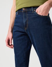 Jeans de mezclilla azul oscuro con costuras en naranja y un ajuste slim, que presentan un bolsillo frontal y un botón de metal en la cintura.