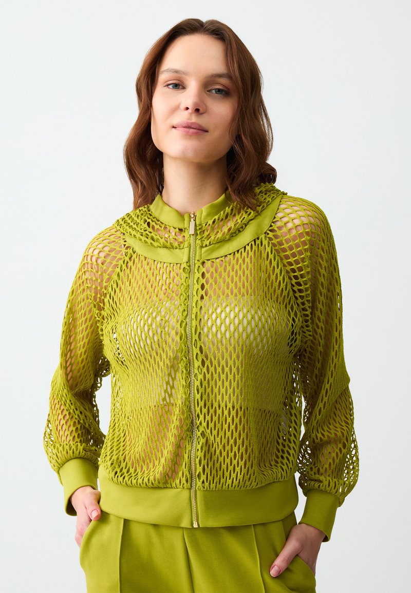 Limegrüne Mesh-Reißverschlussjacke mit hohem Kragen, gerippten Bündchen und einem festen, gefütterten Saum. Verfügt über ein durchsichtiges Muster und eine leichte Textur.