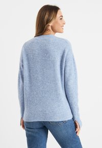 Lichtblauwe gebreide trui van zacht materiaal, met een comfortabele pasvorm, ronde halslijn en geribde zoom, gecombineerd met een spijkerbroek.