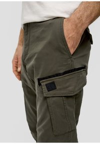 Olive-zelene cargo hlače z več žepi, teksturirano blago, ojačanimi šivi in črnim logotipom na stranehnem žepu.