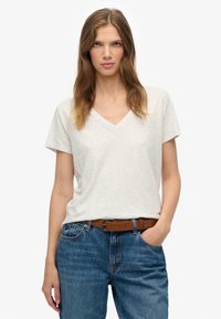 Hellgraues T-Shirt mit kurzen Ärmeln und V-Ausschnitt aus einem weichen, strukturierten Stoff, kombiniert mit blauen Jeans aus Denim und einem braunen Gürtel.