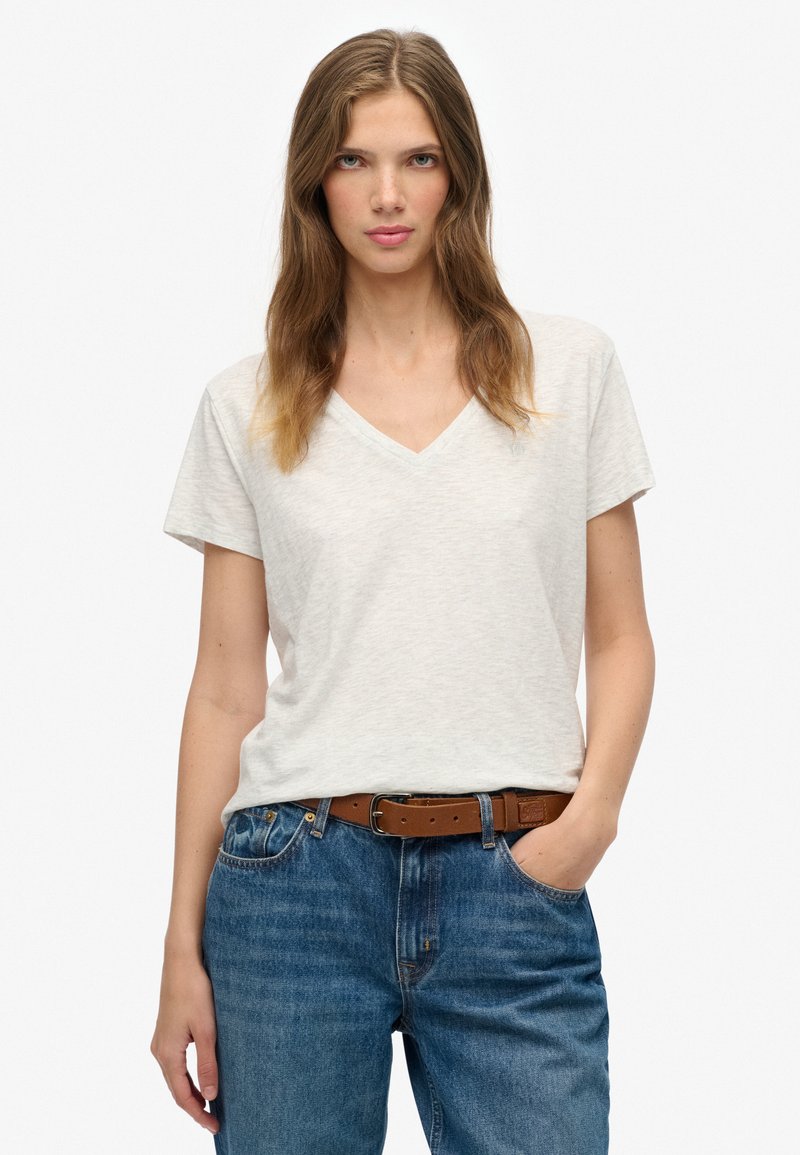 Hellgraues T-Shirt mit kurzen Ärmeln und V-Ausschnitt aus einem weichen, strukturierten Stoff, kombiniert mit blauen Jeans aus Denim und einem braunen Gürtel.