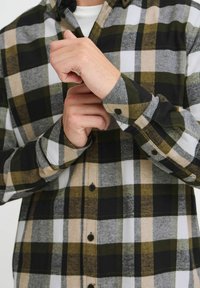 Koszula w kratę z flaneli w czarne, zielone, szare i beżowe kwadraty. Model zapinany na guziki, o miękkiej fakturze z podwiniętymi mankietami.