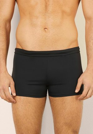 Schwarze Badehosen aus elastischem Material, mit einer mittelhohen Taille und einer glatten Textur ohne sichtbare Muster oder Akzente.