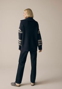 Navy gebreide trui met grote kraag, met patronen op de mouwen, gecombineerd met donkere jeans en grijze instappers, die een relaxte pasvorm toont.
