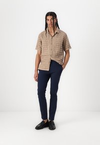 Kortærmet beige skjorte med struktureret mønster, knaplukning foran; sat sammen med mørkeblå slim-fit bukser og sorte loafers.