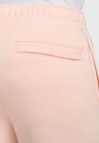 Pantalones de chándal rosa claro con un tejido suave y texturizado, que presenta un bolsillo trasero rectangular y una cinturilla elástica para mayor comodidad.