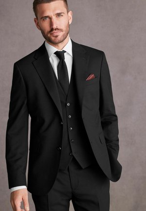 Must mustrikk mustre, millel on slim fit, tähistatud nurgelise krae, kuue nööbiga vest ja punane taskurätt, lisandudes valge särk ja lips.