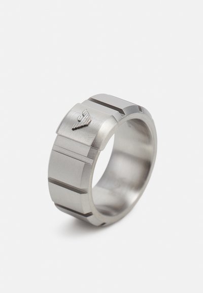 Matte rustfrit stålring med et geometrisk design, der har vandrette spor og et lille præget emblem på den ene side.