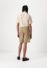 Krátky rukáv, béžová košeľa s_Textúrovanou tkaninou; v kombinácii s khaki šortkami. Čierne topánky dokončia outfit, pohľad zozadu.
