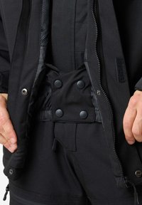 Schwarze Oberbekleidung mit einem Reißverschluss vorne, Druckknopfverschluss, elastischem Bund und Mesh-Futter; glatte, matte Textur mit subtilen Akzenten.