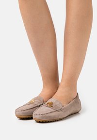 Pair of taupe suede loafers with gold "RL" logo worn on feet against a plain white background.