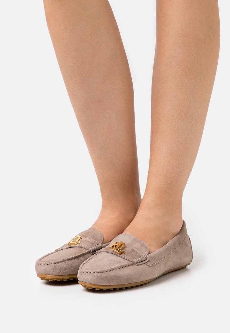 Pair of taupe suede loafers with gold "RL" logo worn on feet against a plain white background.