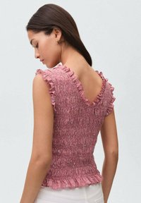 Top rosa con arricciature e maniche a volant, con design a V sul retro. Tessuto caratterizzato da volant e silhouette aderente, realizzato in tessuto leggero.