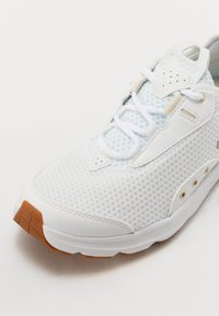 Białe siatkowe buty sportowe z jasnoniebieskimi akcentami, z wyściełanym kołnierzem, sznurowanym zapięciem i brązową gumową podeszwą zapewniającą przyczepność.