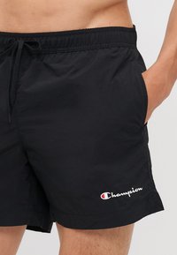 Shorts de bain noirs en tissu léger. Dotés d'une taille élastique avec cordon de serrage et de poches latérales. Logo brodé sur la jambe.