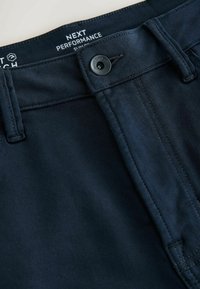 Vita di jeans slim fit blu navy che mostra il bottone con il marchio "Denim Supply Co" e l'etichetta "NEXT Performance Slim".