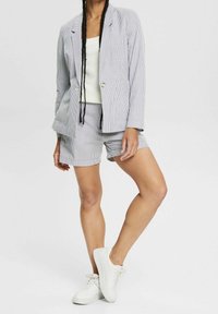 Ensemble blazer à rayures et short assorti en bleu clair et blanc, confectionné dans un tissu léger. Débardeur blanc et baskets blanches décontractées.